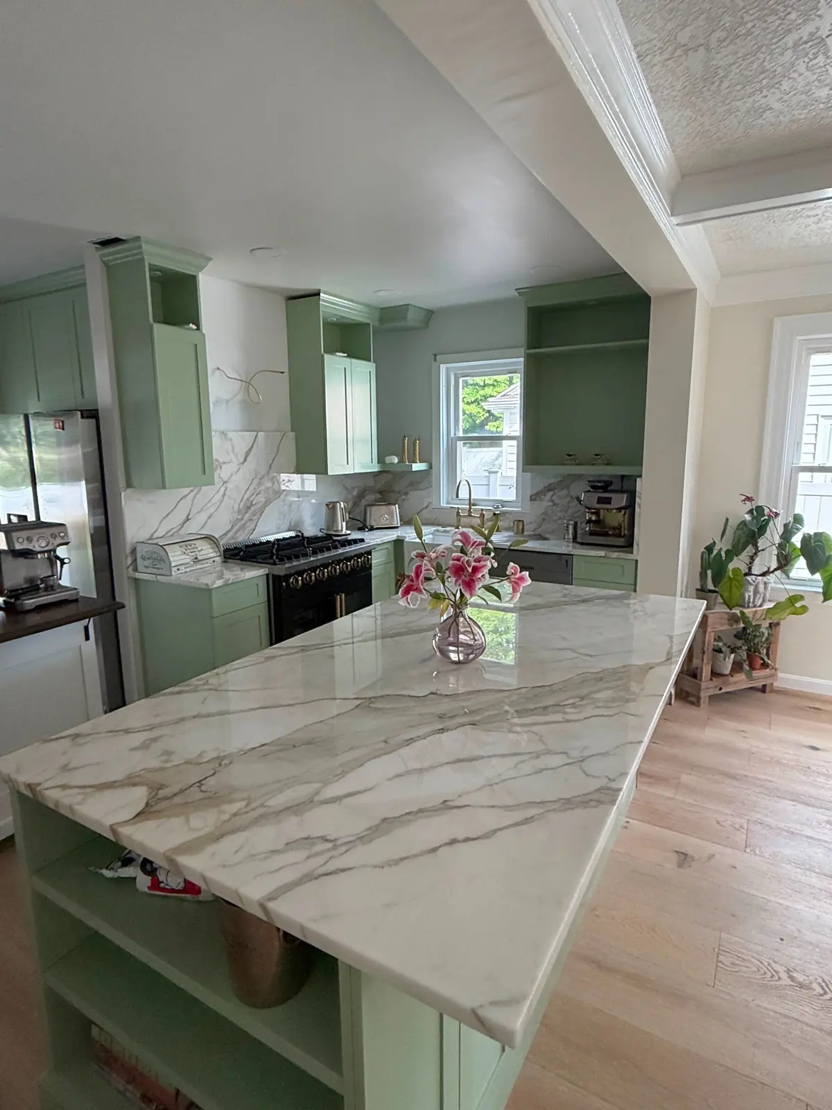 Veined stone kitchen island and matching backsplash with green cabinetry